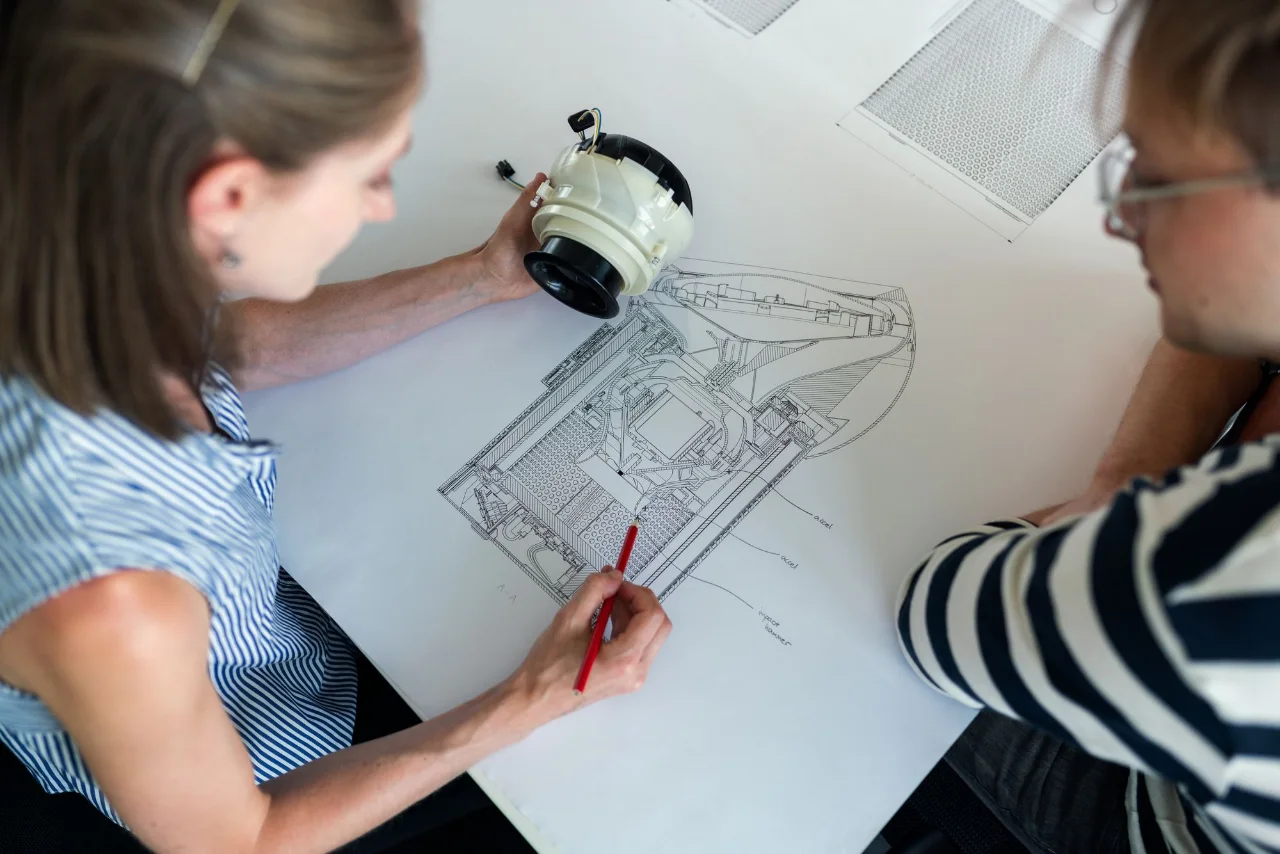 Engineers reviewing a physical component over an equipment drawing