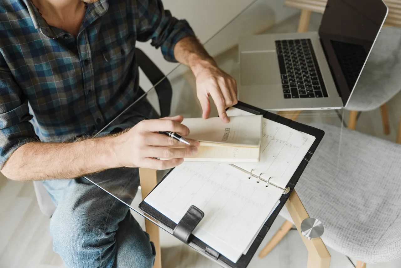 Person making notes in a planner beside a laptop
