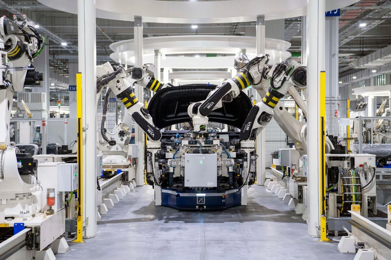 Industrial robot arms surrounding a vehicle in a bright automotive factory