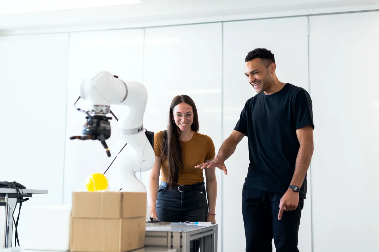 Two engineers working beside a robotic arm in a laboratory